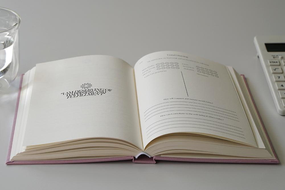 Open journal displaying affirmations with a glass of water visible in the background on a clean white surface 